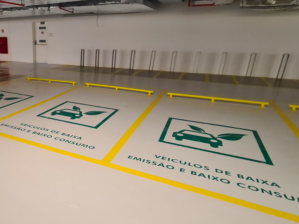 Vagas de estacionamento internas com piso epóxi claro e sinalização verde indicando área para veículos de baixa emissão e baixo consumo.