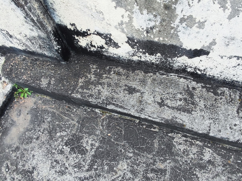 Área externa com piso envelhecido e desgastado, apresentando infiltração e sinais de deterioração junto ao rodapé.