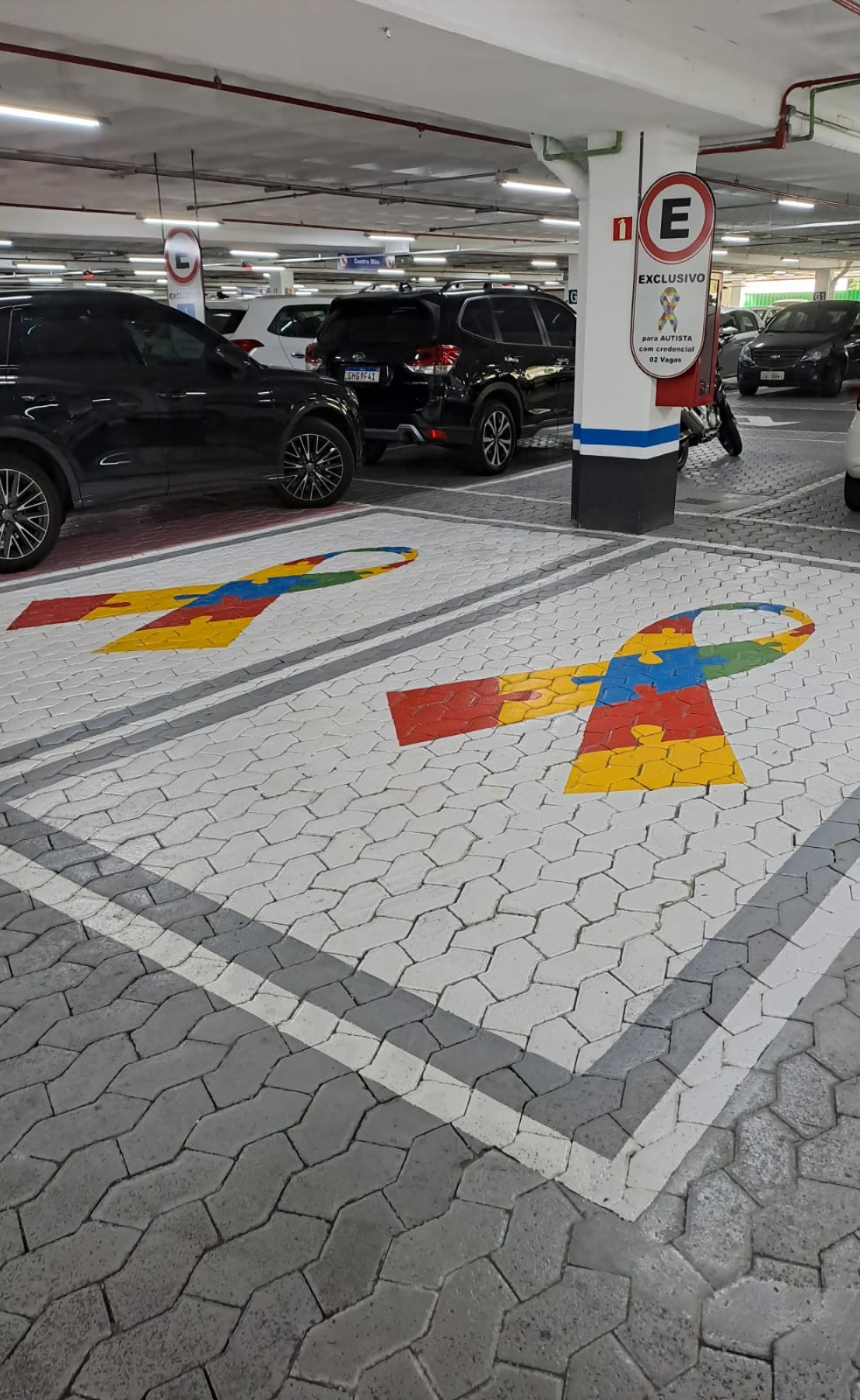 Vagas de estacionamento com blocos intertravados claros e pintura de laços coloridos representando o autismo.