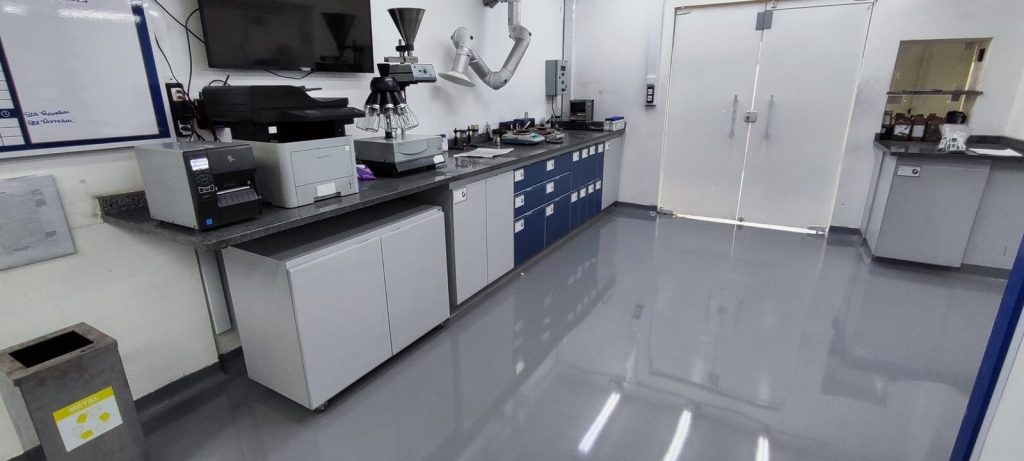 Laboratório industrial com piso epóxi cinza brilhante, bancadas equipadas com instrumentos e armazenamento organizado.