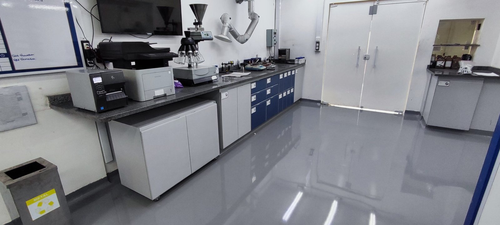 Laboratório industrial com piso epóxi cinza brilhante, bancadas equipadas com instrumentos e armazenamento organizado.