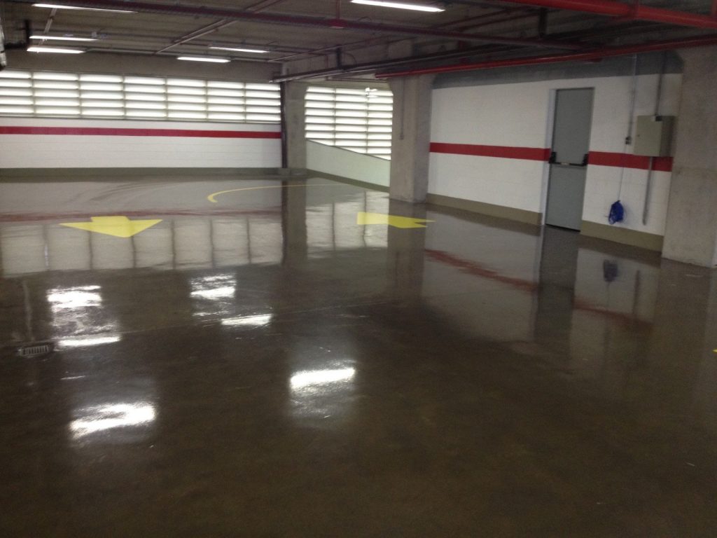 Estacionamento interno com piso polido escuro e setas amarelas indicando o sentido de tráfego.