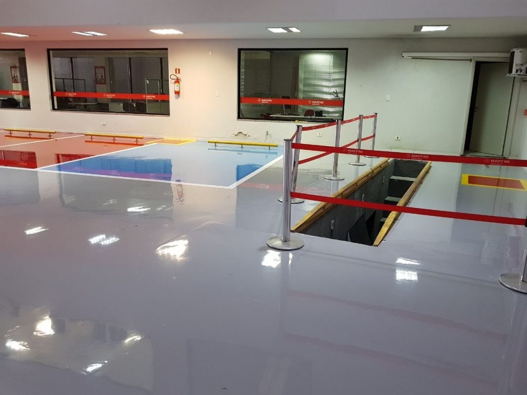 Ambiente interno com múltiplas áreas demarcadas em cores epóxi diferentes refletindo luz, separado por barreiras de segurança.