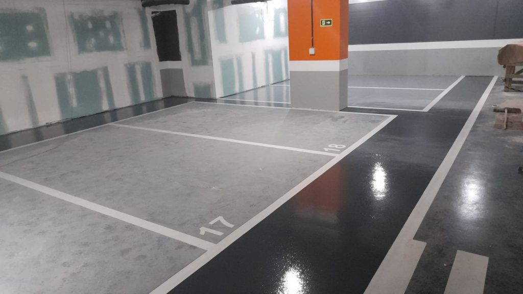 Estacionamento interno com pintura epóxi cinza e preta, marcações brancas e numeração de vagas recém-executadas.