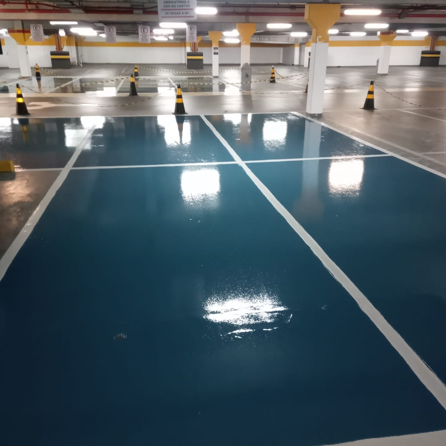 Vaga de estacionamento com pintura epóxi azul brilhante e marcações brancas recém-aplicadas.