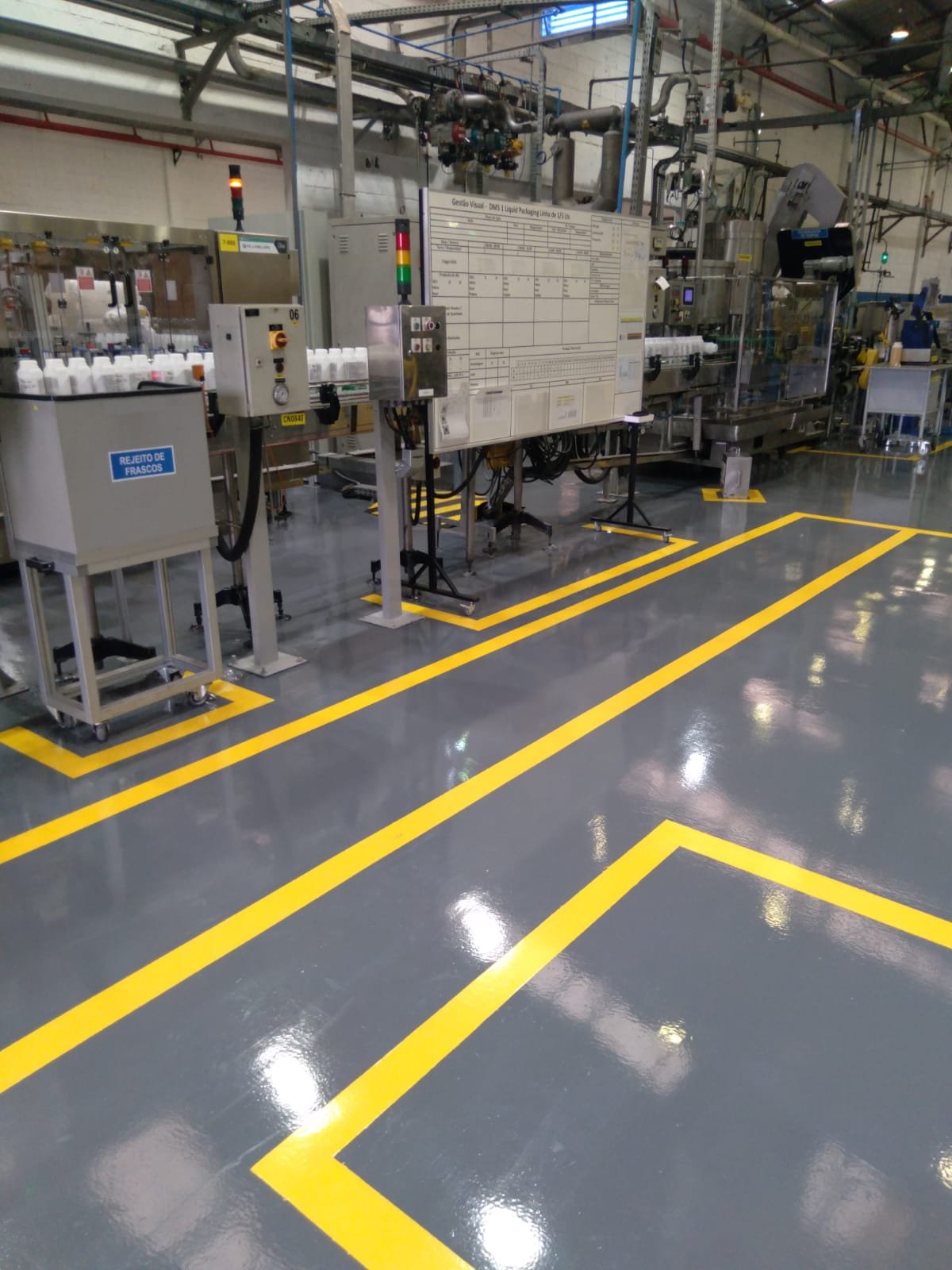 Piso epóxi cinza brilhante em área industrial, com demarcações amarelas bem definidas em volta de máquinas e painéis.