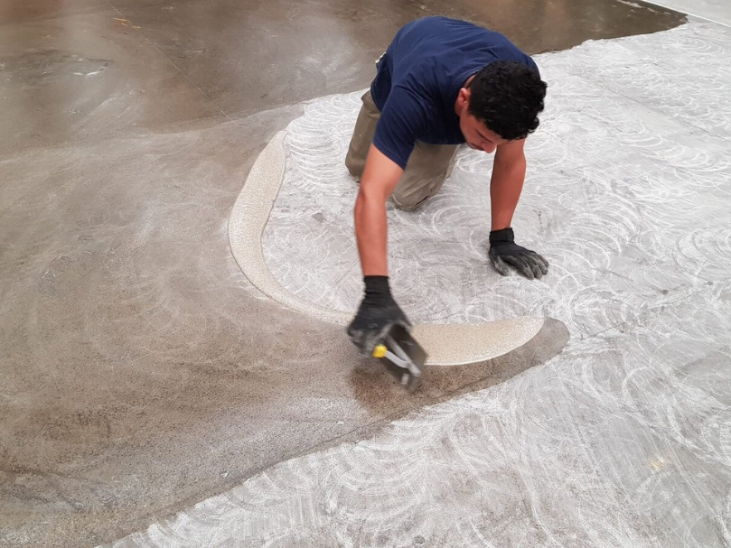 Trabalhador aplicando massa de regularização no piso com desempenadeira, preparando a superfície para receber revestimento.