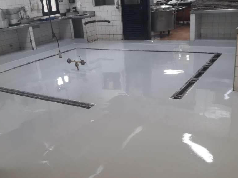 Cozinha industrial com piso epóxi cinza recém-instalado, apresentando ralos lineares e áreas niveladas para higienização.