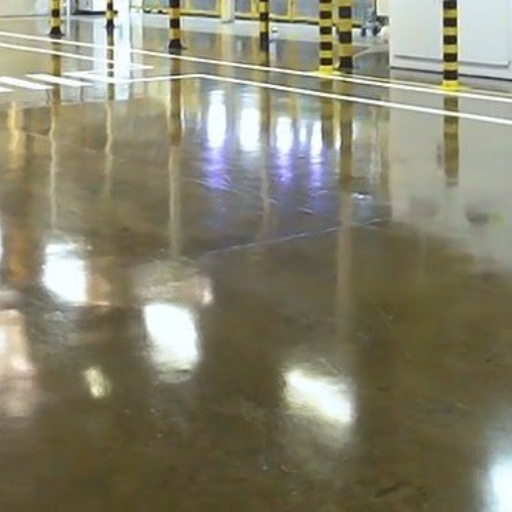 Área industrial com piso polido brilhante e colunas marcadas em amarelo e preto para segurança.