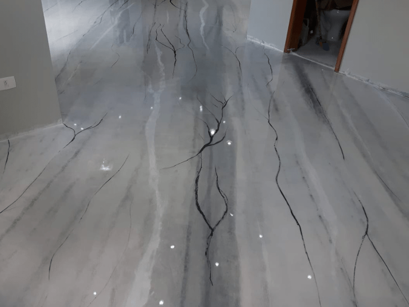 Ambiente residencial com piso epóxi marmorizado em tons de cinza e veios escuros, acabamento alto brilho.
