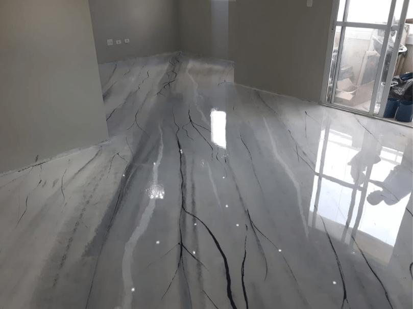 Sala residencial com piso epóxi marmorizado em tons de cinza e veios escuros, acabamento brilhante.