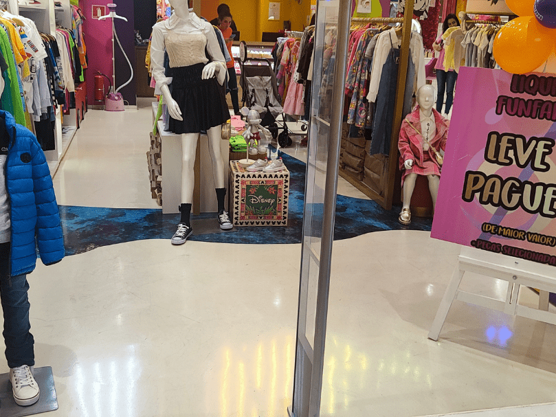 Entrada de loja infantil com piso epóxi branco combinado com detalhes azuis decorativos, manequins e exposição de roupas.
