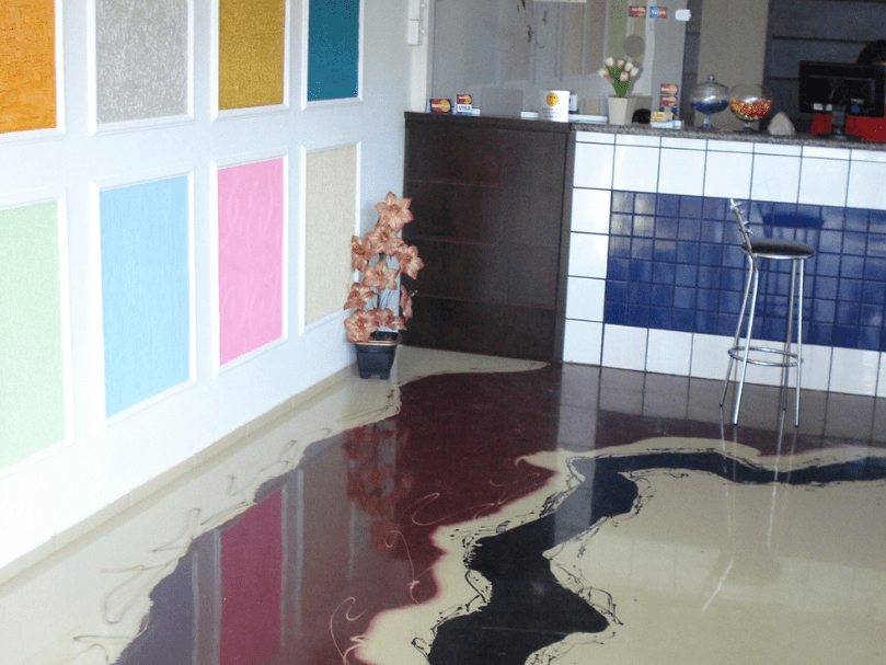 Recepção com piso epóxi artístico em tons de vinho, bege e preto, formando efeito marmorizado junto a parede decorativa multicolorida.