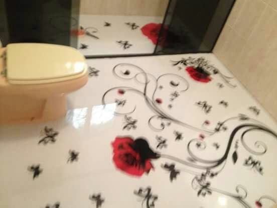 Banheiro com piso epóxi 3D branco decorado com rosas vermelhas e arabescos pretos, ao lado de vaso sanitário.