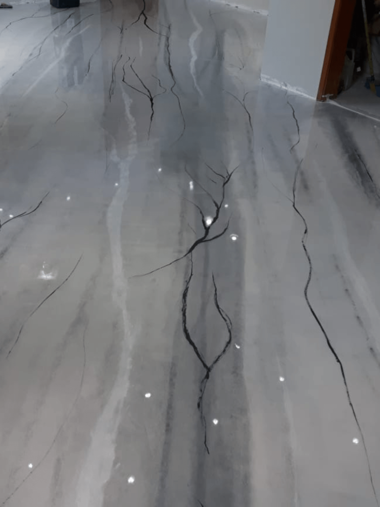 Piso epóxi decorativo com efeito marmorizado em tons de cinza e veios escuros, acabamento brilhoso.