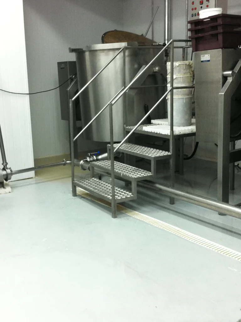 Piso epóxi claro em indústria alimentícia com escada e equipamentos em inox.