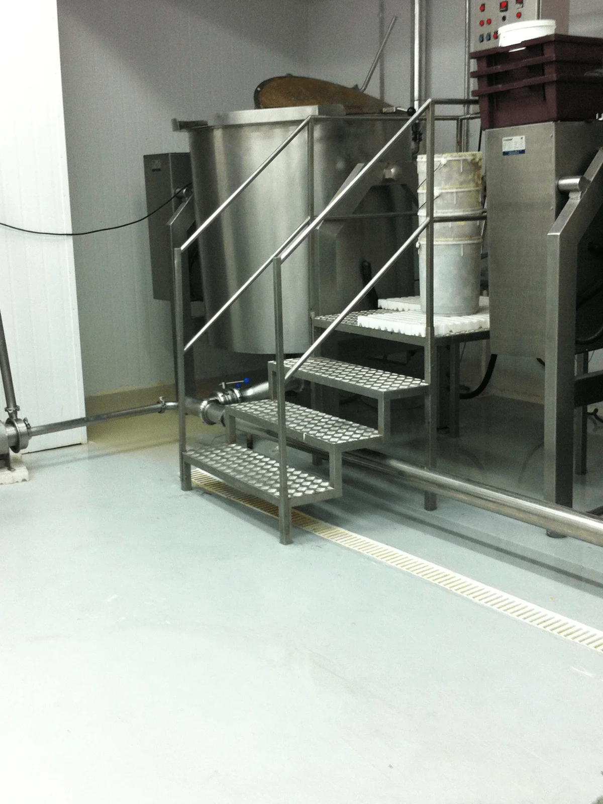 Piso epóxi claro em indústria alimentícia com escada e equipamentos em inox.