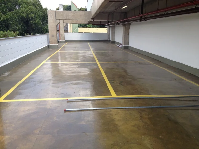 Estacionamento externo com piso polido brilhante e faixas amarelas, sob estrutura de concreto aberto.