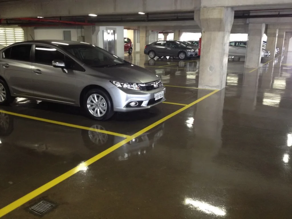 Estacionamento interno com piso de concreto polido brilhante, marcado com linhas amarelas e carros estacionados.