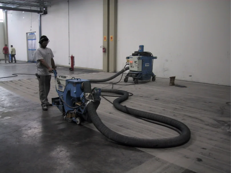 Operador utilizando máquina de jateamento (shot blasting) para preparo de piso industrial.