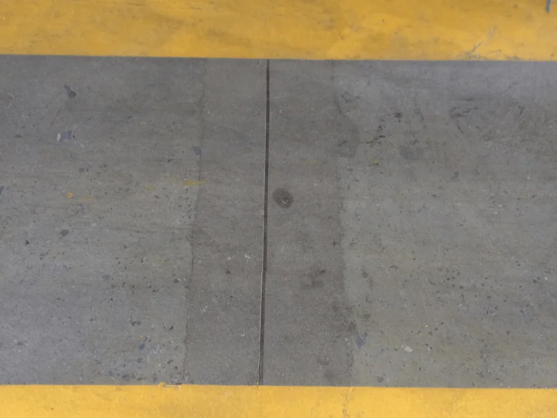Junta de dilatação em piso de concreto com faixa amarela na parte superior, mostrando desgaste e alteração de tonalidade no material.