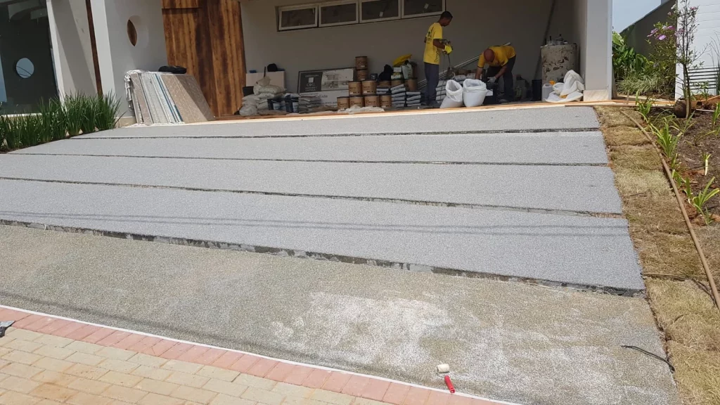 Rampa residencial sendo revestida com sistema granilite/quartzo, com fileiras aplicadas e equipe trabalhando ao fundo.