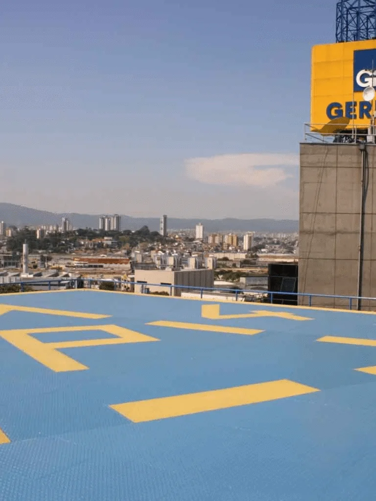 Heliponto elevado com pintura azul e marcas amarelas, mostrando vista panorâmica da cidade ao fundo.