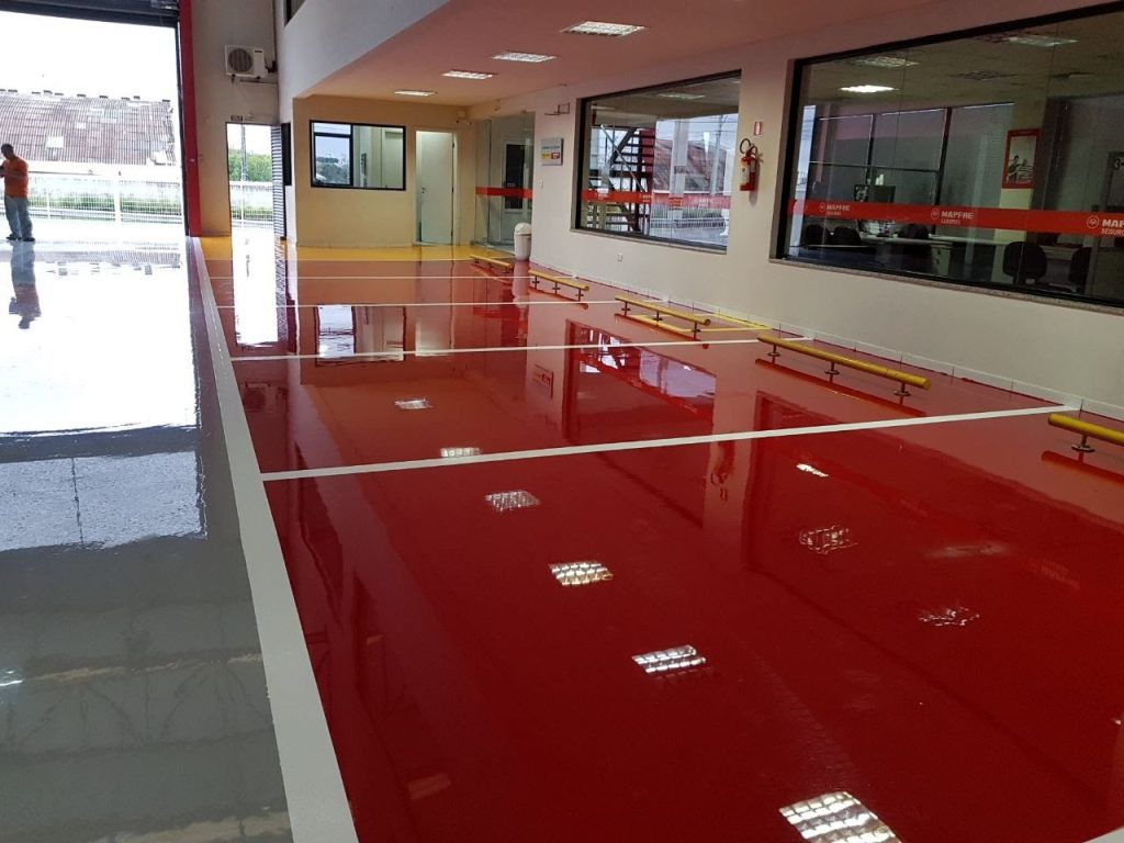 Área de atendimento automotivo com piso epóxi vermelho e cinza, acabamento brilhante e divisões marcadas.