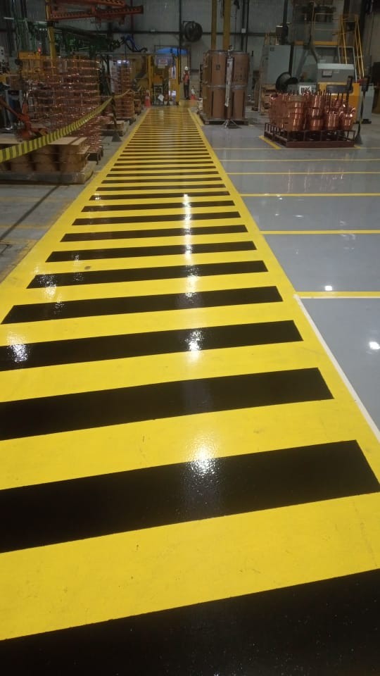 Passarela industrial com pintura de segurança em faixas amarelas e pretas recém aplicada.