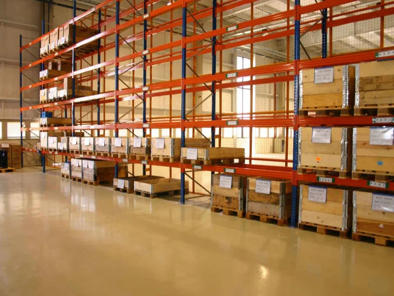 Estantes metálicas altas com gavetas e caixas de madeira organizadas sobre um piso industrial claro e liso.