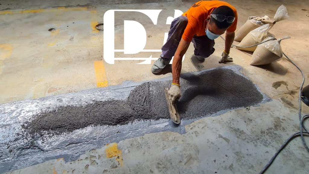 Operário aplicando argamassa epóxi ou reparo de piso industrial.