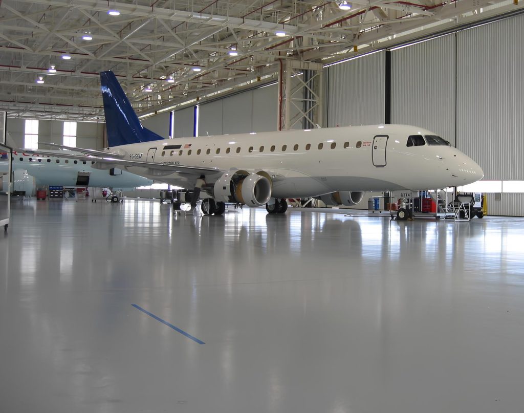 Avião em hangar industrial com piso epóxi cinza claro altamente reflexivo e ambiente amplo iluminado.