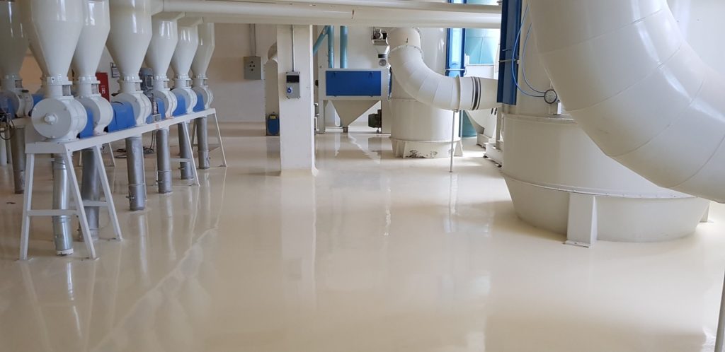 Setor industrial com piso epóxi creme brilhante, tubulações e máquinas de grande porte.