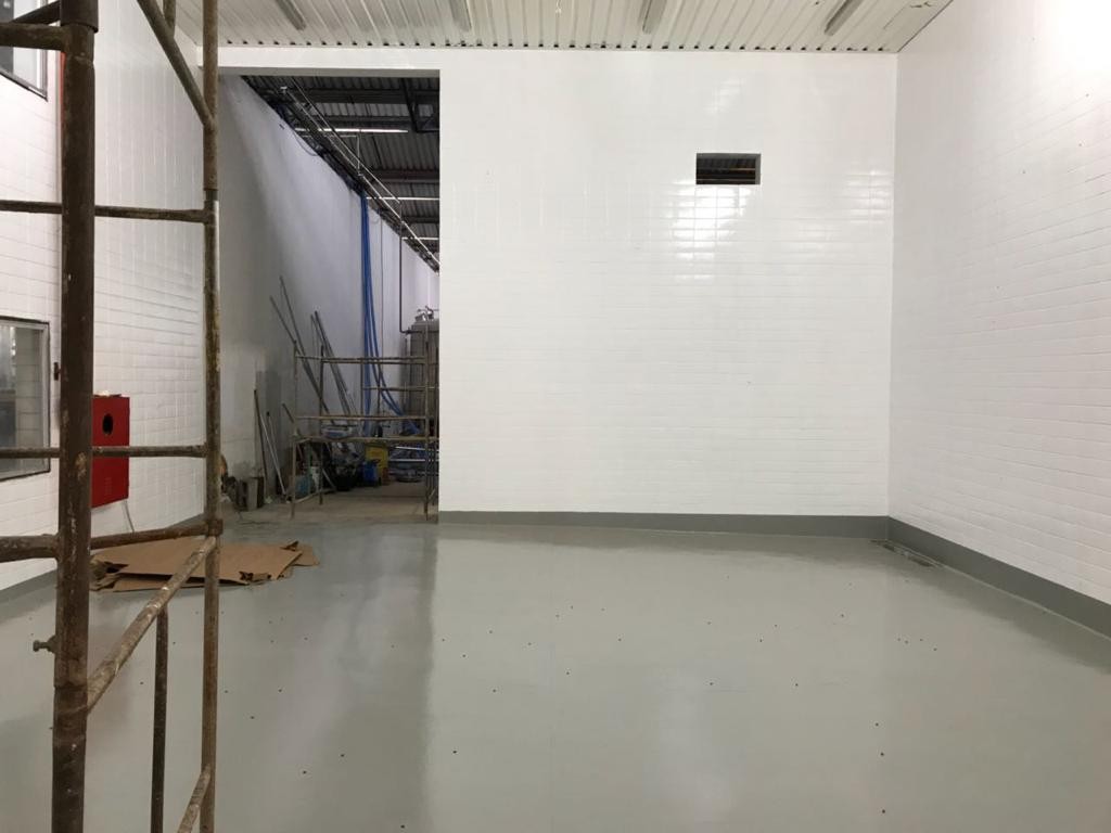 Sala industrial com paredes de azulejo branco e piso epóxi cinza finalizado, com andaime ao lado.