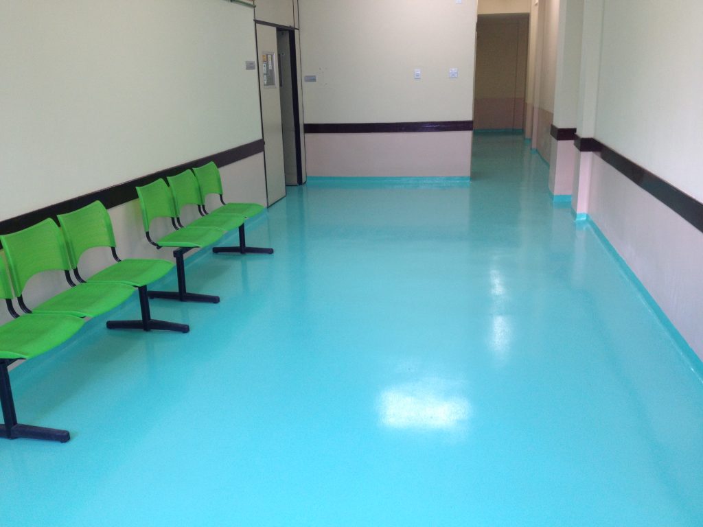 Sala de espera hospitalar com piso epóxi azul e cadeiras verdes encostadas à parede.