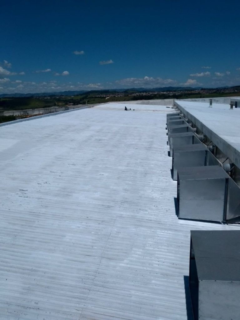 Cobertura metálica industrial pintada com revestimento branco reflexivo, vista ampla sob céu azul.