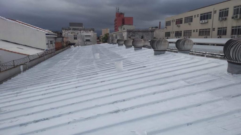 Cobertura metálica com impermeabilização branca refletiva e exaustores eólicos alinhados sobre o telhado.