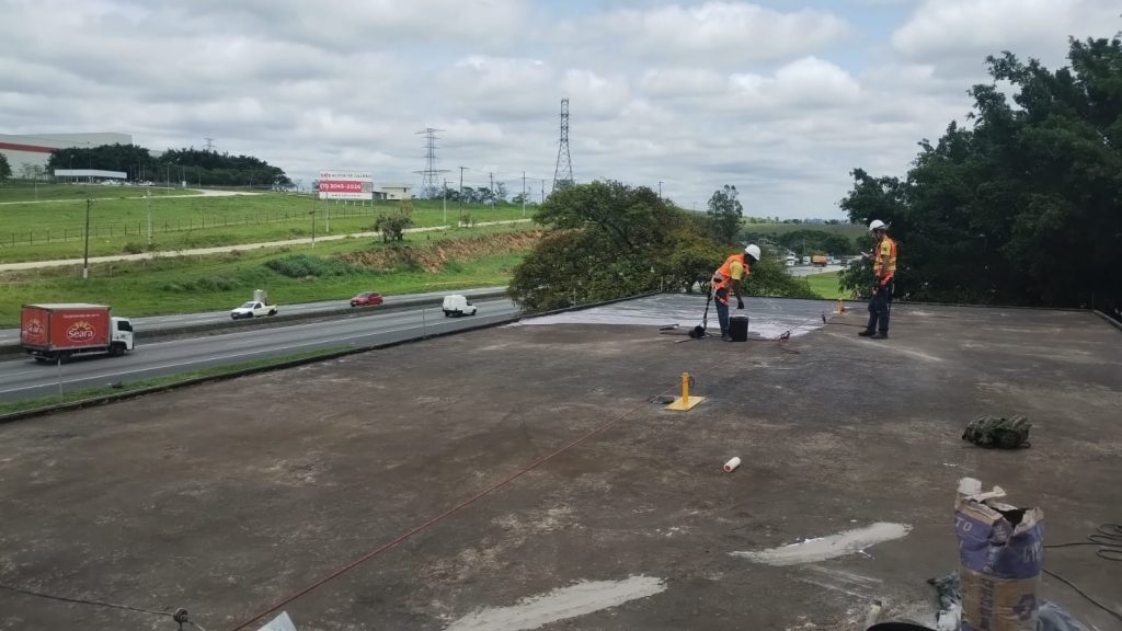 Profissionais iniciando a preparação do telhado industrial escurecido, removendo sujeira e resíduos antes da impermeabilização.